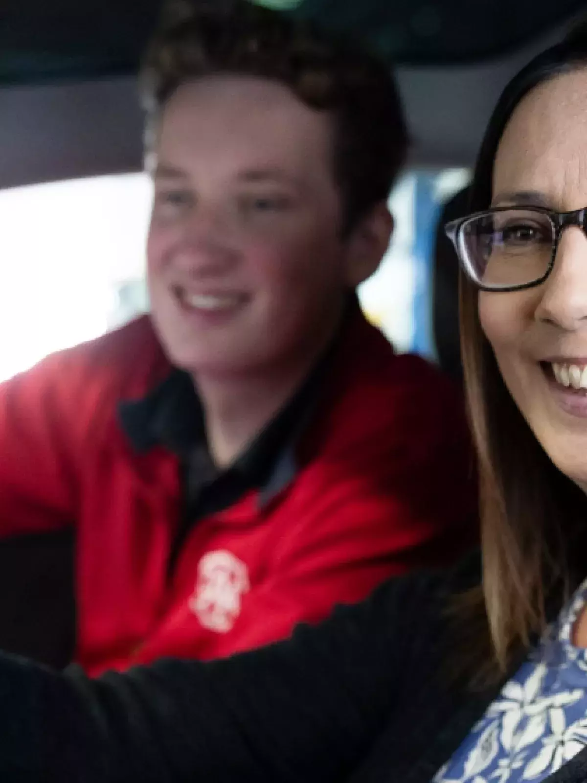 woman in the drivers seat wearing glassess smiling out the window with a CAA representative in a red shirt smiling in the passenger seat