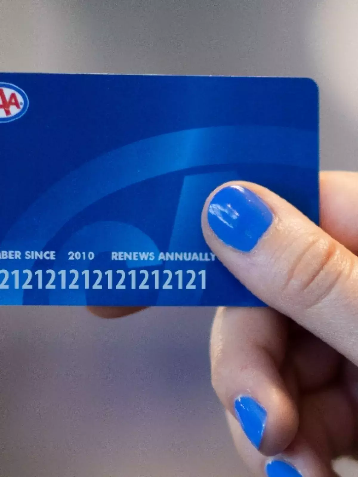 hand with blue nailpolish holding a blue CAA membership card with the CAA logo at the top left 