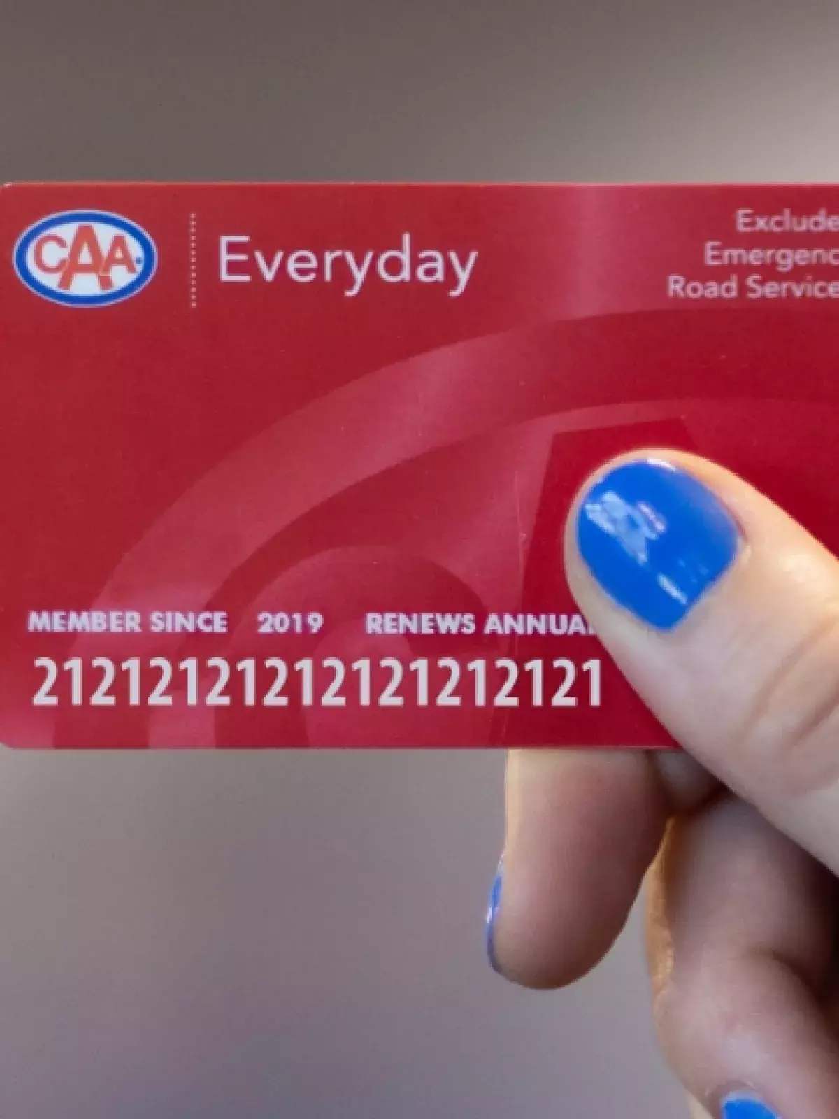 hand with blue nailpolish holding a red CAA membership card with the word Everyday at the top left to the right of the CAA logo. Top right of the card says Excludes Emergency Road Services
