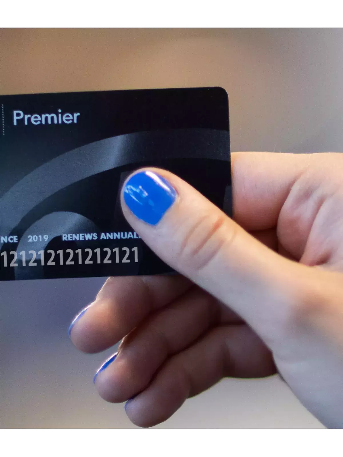 hand with blue nailpolish holding a black CAA membership card with the word Premier listed at the top to the right of a CAA logo