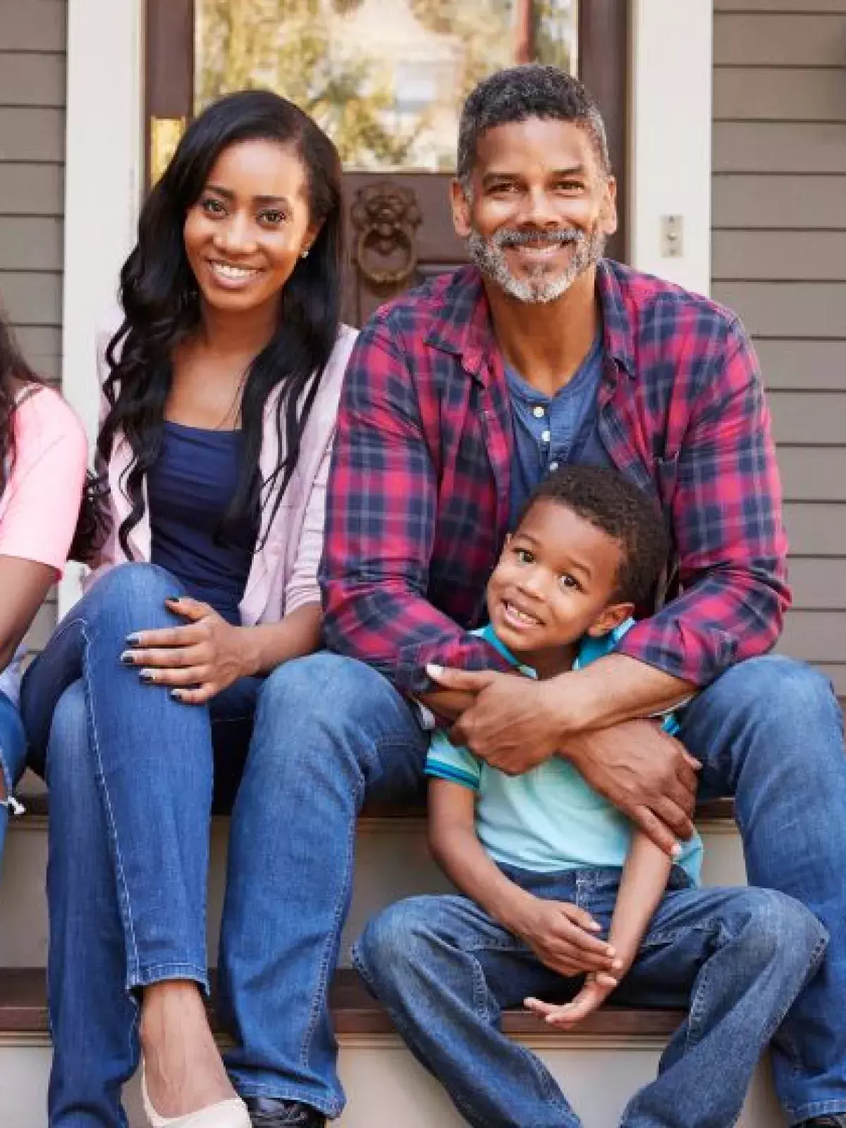 Family of four sits on the front step of their house with their white dog. 
