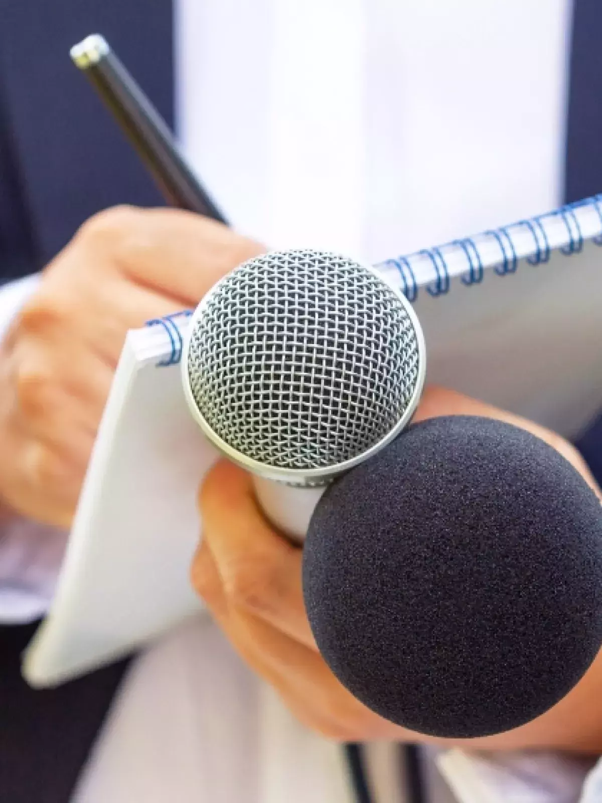 Close up shot of a man in a suit holding a pad, paper and a microphone