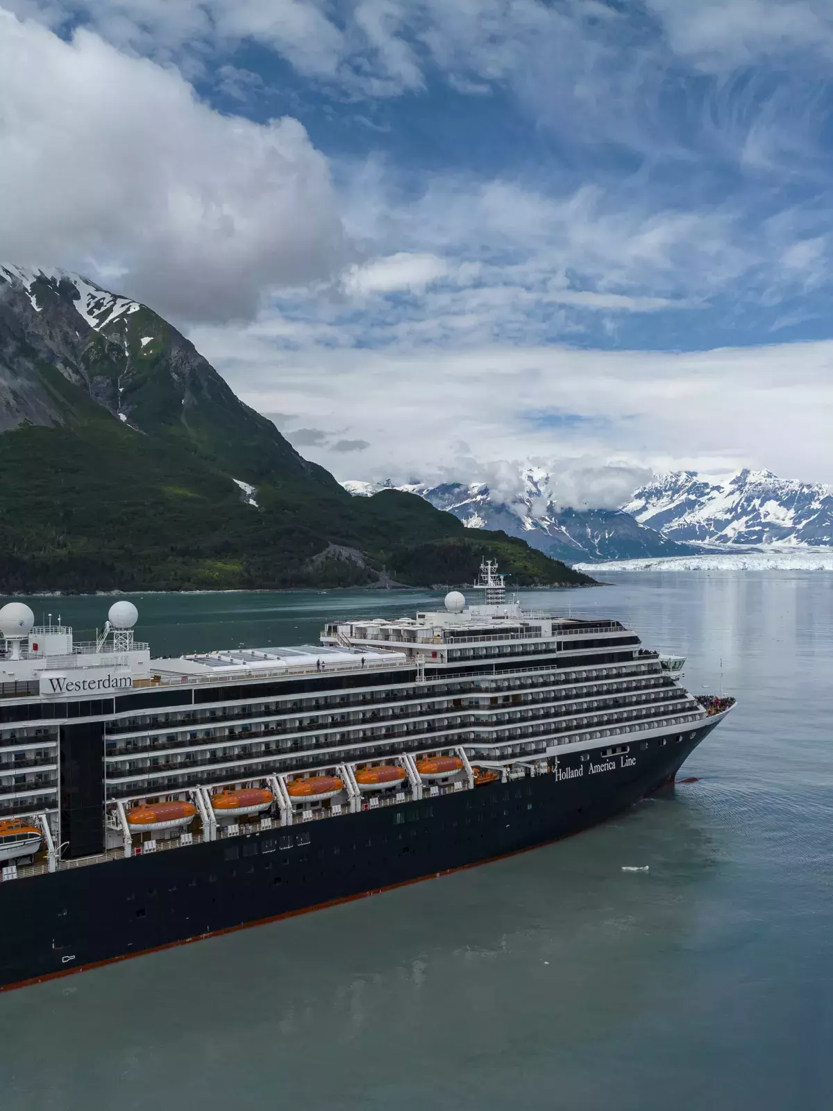 A Holland America Line cruise ship sails past mountains and glaciers.