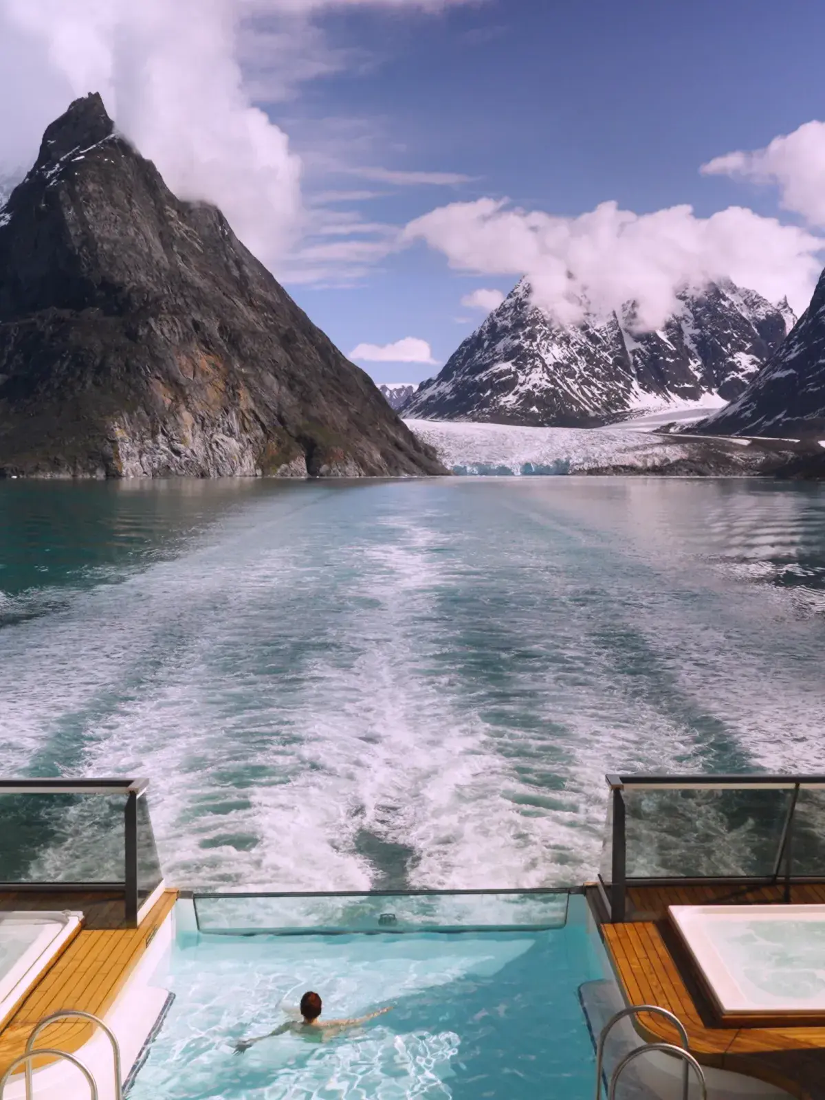 Cruise ship hot tubs overlooking turquoise water and snow-covered mountains with a glacier.