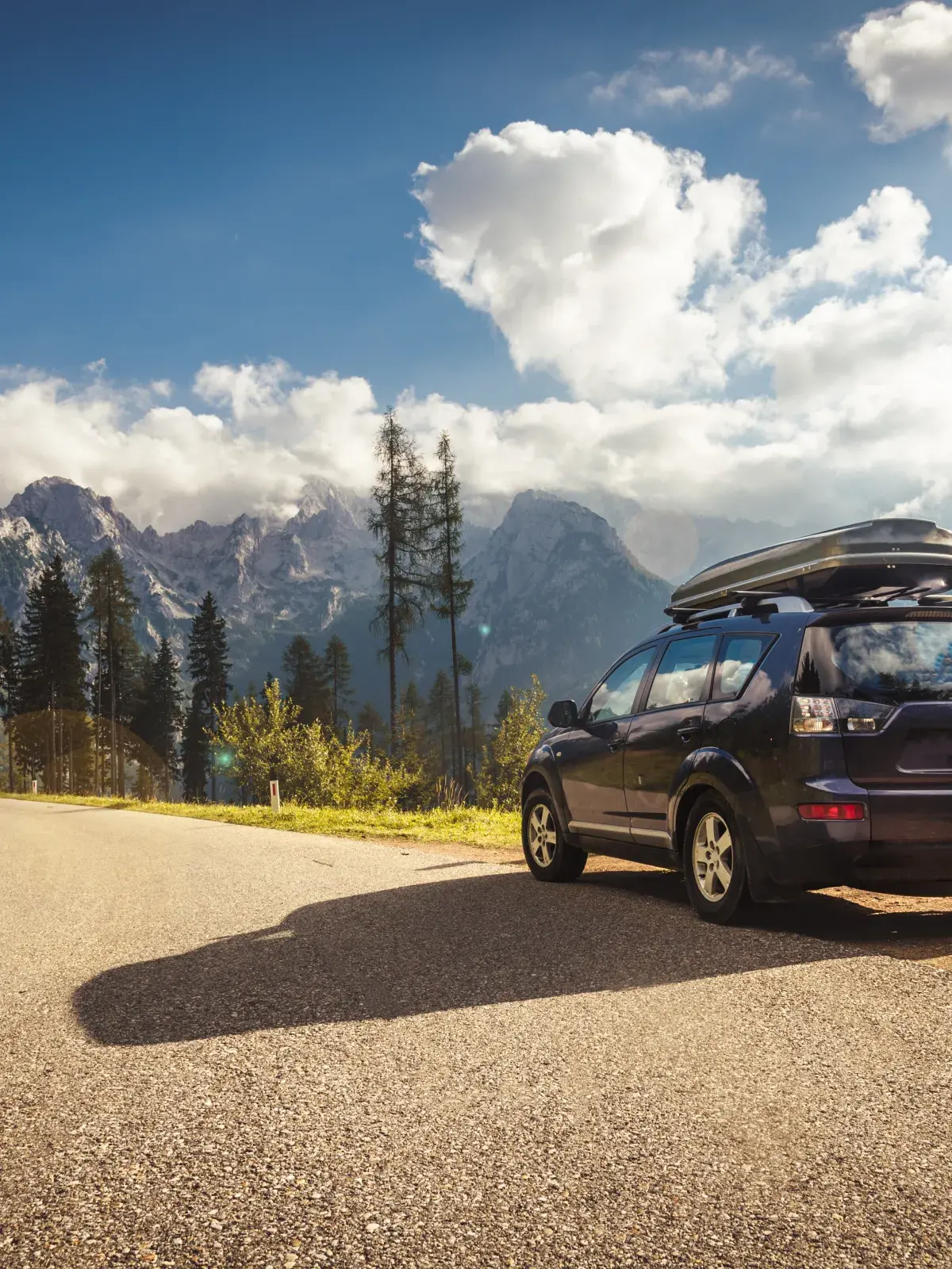  SUV parked on a winding mountain road with forested peaks and blue sky in the background.