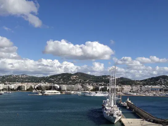 The image shows a scenic coastal view of a marina with a large sailboat docked near a pier.