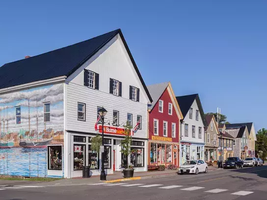 Colorful street in St. Andrews with shops, a boat-themed mural, parked cars, and a clear blue sky.