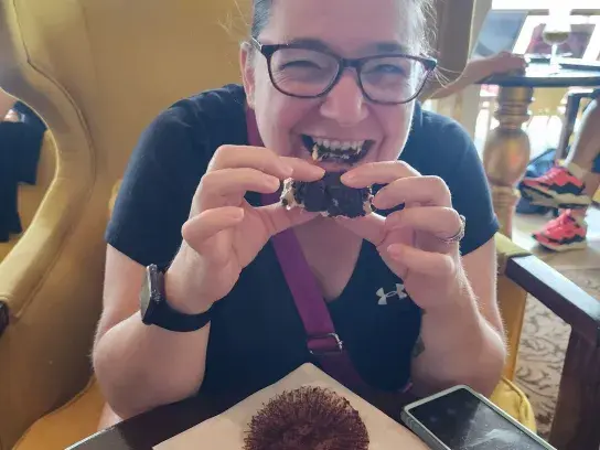 Tanya sitting indoors at a table eating a dessert and smiling.