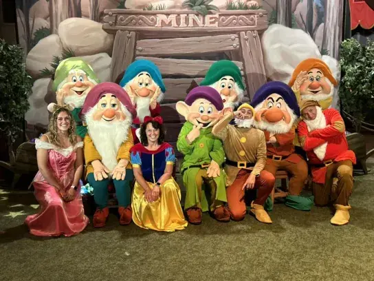 Linda posing with Snow White and the Seven Dwarfs characters in a themed fairytale attraction.