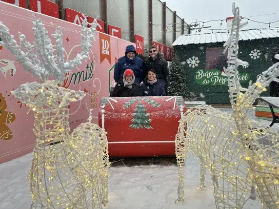 Group posing beside a festive sleigh display surrounded by illuminated reindeer decorations during a snowfall.