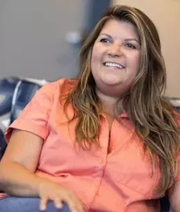 close up shot of a woman smiling wearing an orange tshirt sitting in a chair