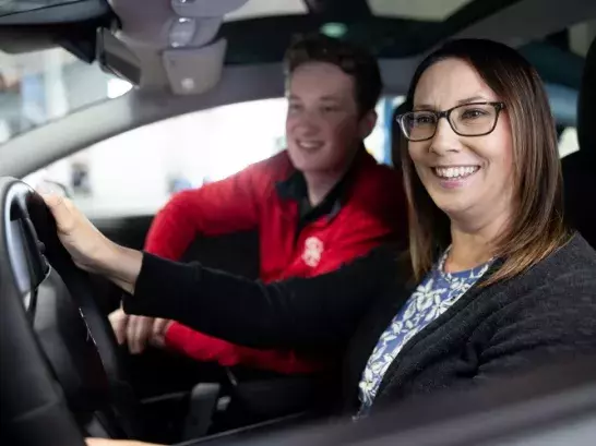 Man and woman sititng in the passenger and driver seat respectively, smiling out the driver seat window. 