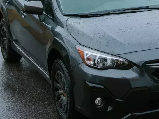 Close up image of the front right of a dark green subaru with rain pellets