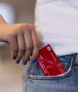 hand with blue nailpolish pulling out a red everyday membership card out of blue jeans pocket