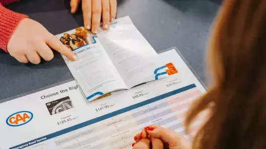 Person pointing to a pamphlet on a table on top of a chart outlining membership plans