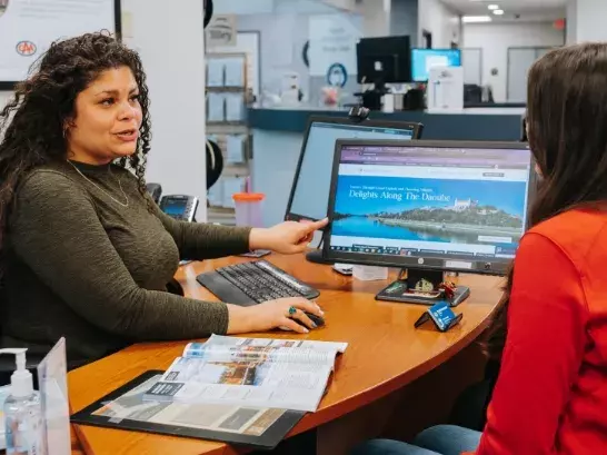 Two women looking at a computer screen, with one woman showing the other a destination on the computer