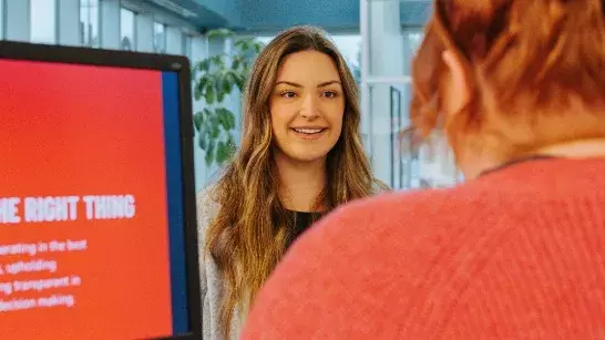 Young lady smiling at an attendant wearing a red sweater behind a computer screen