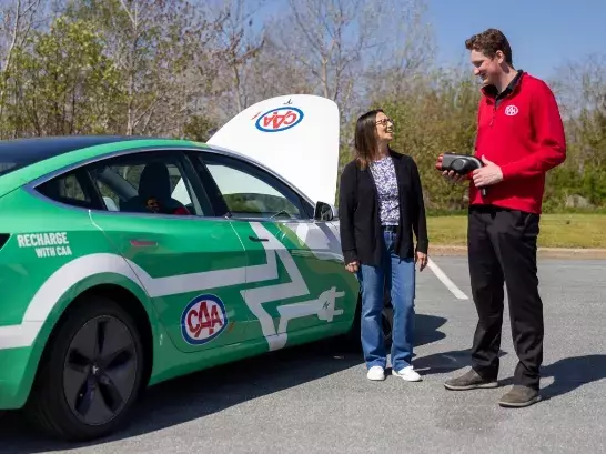 A woman standing next to a CAA worker holding onto an EV charger. Both standing next to a EV with the hood up