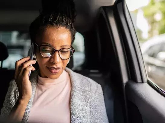 Woman in the passenger seat of a car wearing glasses talking on the phone