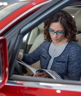 A brown-haired woman siters in her car and reads a brochure