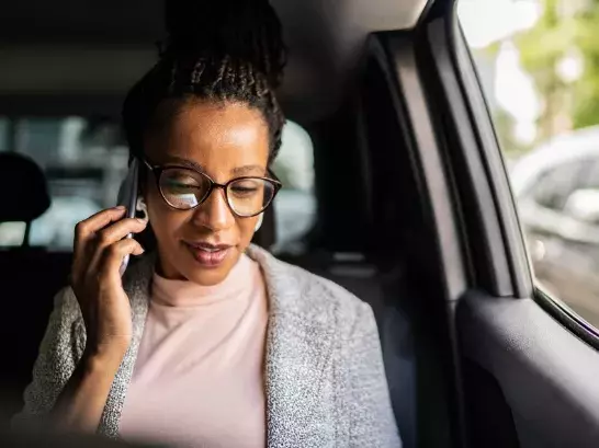 Woman in the passenger seat of a car wearing glasses talking on the phone