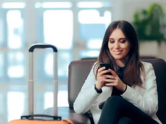 Woman sitting in a chair smiling looking down at her phone wiht a suitcase next to her