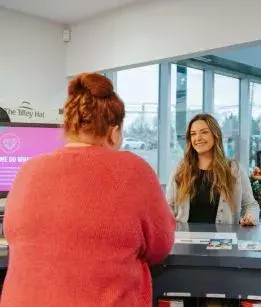 Woman at a CAA branch speaking to a CAA employee at hte customer service counter. 