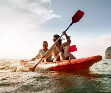 A male and female couple on a red kayak paddling against a sunset