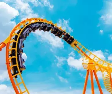 View of a roller coaster against a blue sky with white clouds while riders are upside down going through a loopdy loop