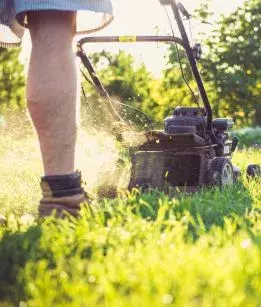 A man pushes his lawn mower through the grass