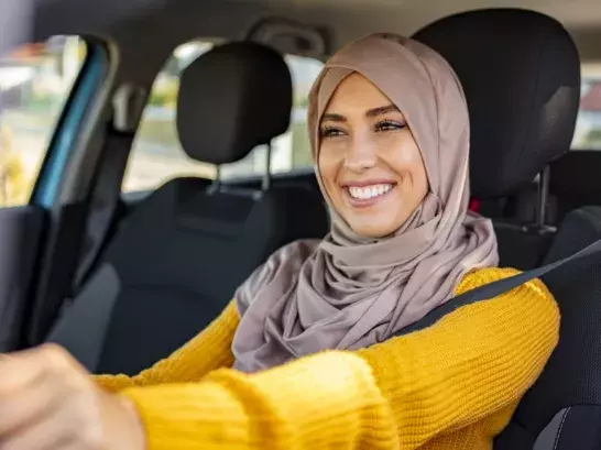 Woman wearing a hijab smiling in the drivers seat of a car