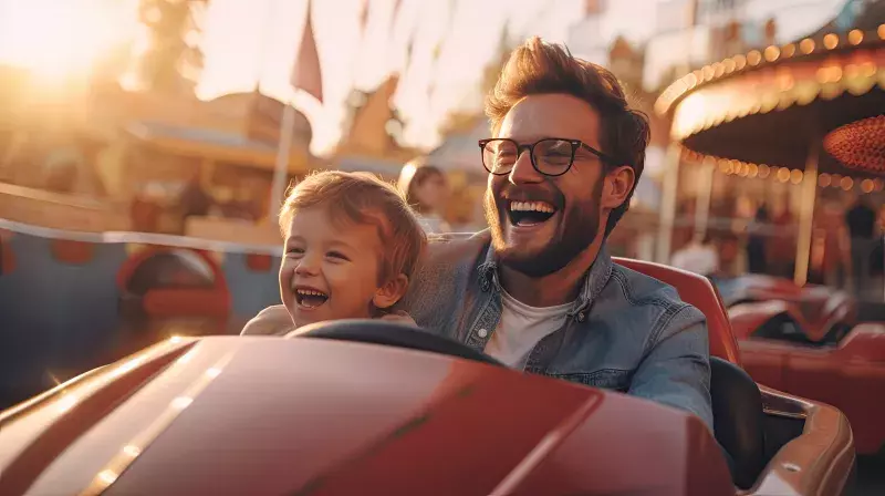 Cheerful father and son and have fun while driving a bumper car in an amusement park. 