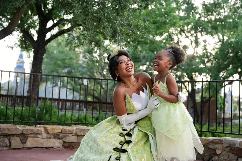 A young girl and Tinkerbell embrace in front of the Magic Kingdom