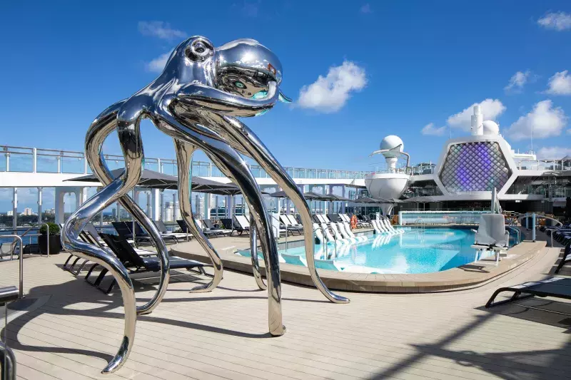 The top deck of the Celebrity Cruise ship. There is a pool and a silver sculpture.