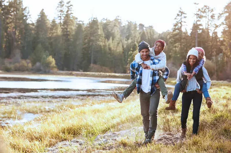 Family of four walking. The parents are giving their children piggyback rides.