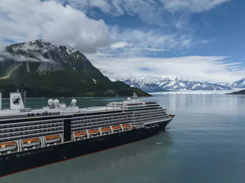 A Holland America Line cruise ship sails past mountains and glaciers.