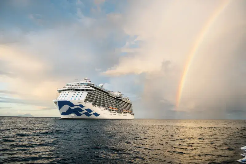 A Princess Cruise ship on the water with a rainbow beside it.