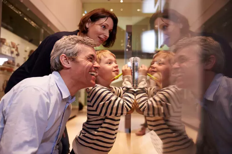 Three people looking at a reflective surface with mirrored reflections.
