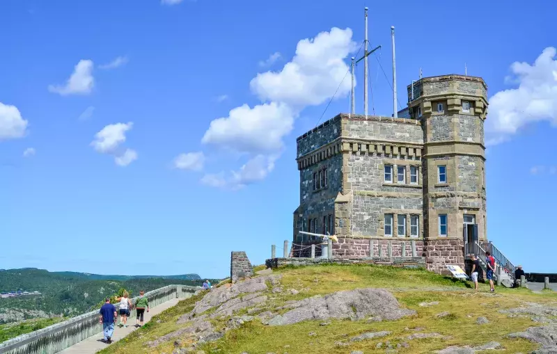 Stone tower on Signal Hill in Newfoundland, with people walking nearby and green hills in the background under a partly cloudy sky.
