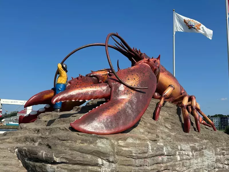 Large lobster sculpture in Shediac with a person beside it, flags in the background, and a clear blue sky.
