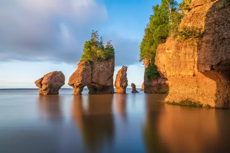 Hopewell Rocks in the Bay of Fundy, with tree-topped formations surrounded by calm water under a partly cloudy sky.