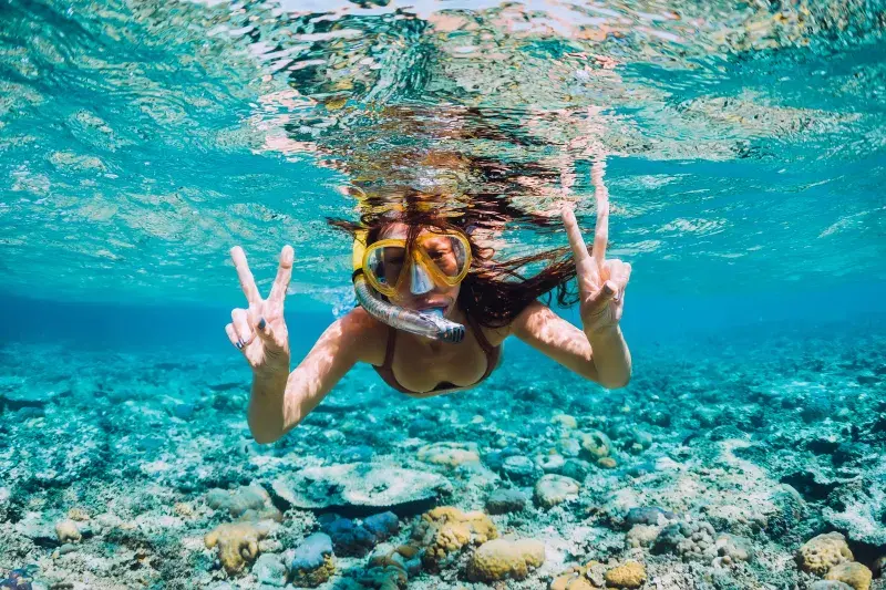 Snorkeler making peace signs above a vibrant coral reef.