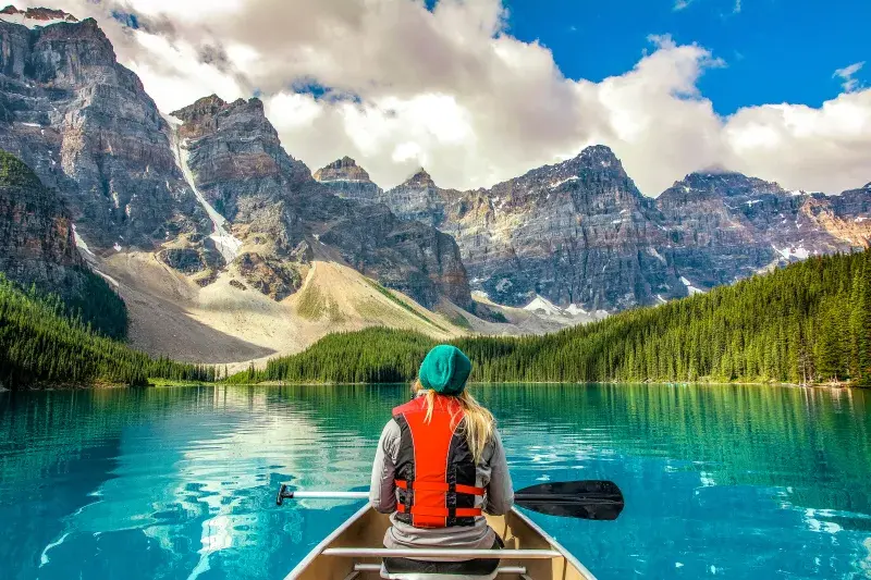 A person paddles a canoe on Moraine Lake in Banff National Park, Canada, surrounded by towering mountains and crystal-clear water.