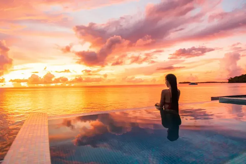 Person at infinity pool watching a colorful ocean sunset.