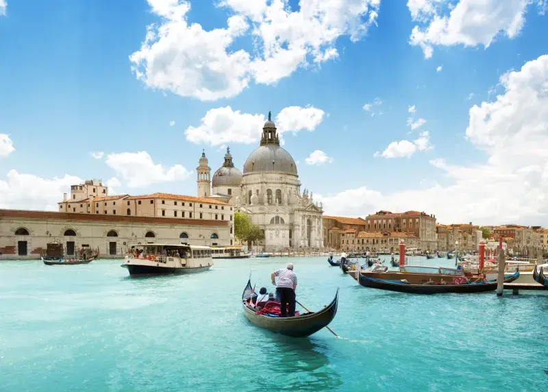 Gondolas float on a canal in Venice, Italy, with the Santa Maria della Salute church visible in the background.