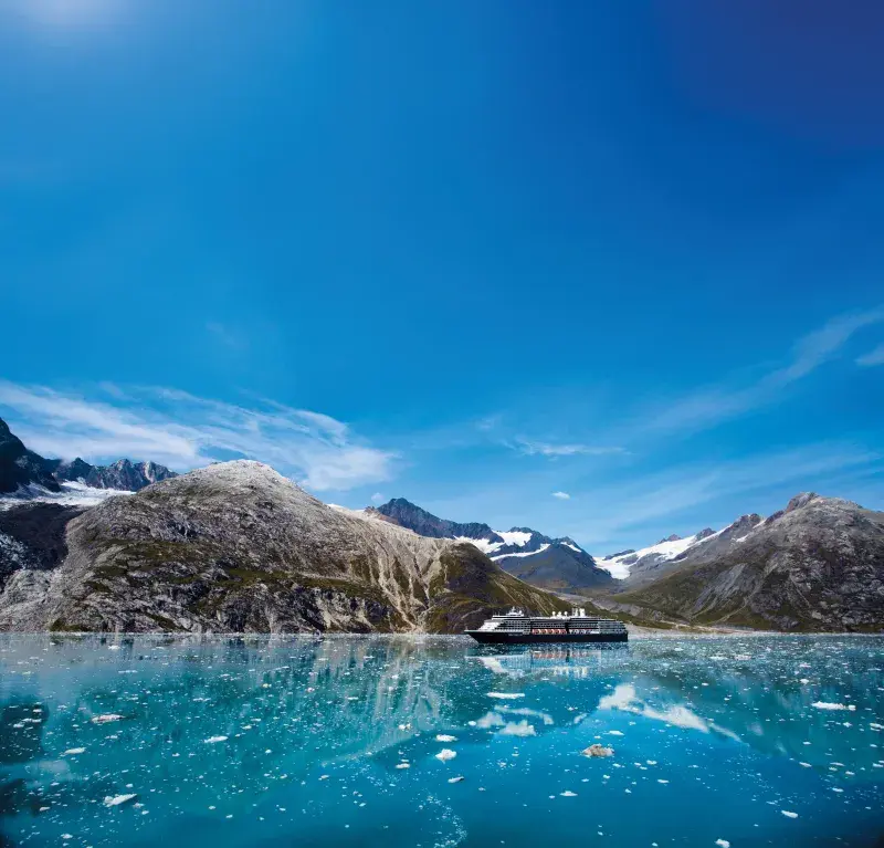 Cruise ship sailing in Glacier Bay with snow-capped mountains and icy blue water under a clear sky.