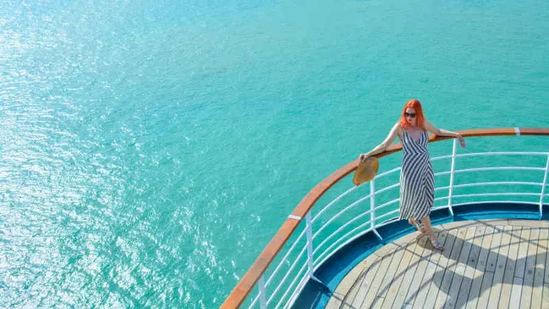 Woman in a striped dress stands on a ship’s deck overlooking turquoise ocean water.