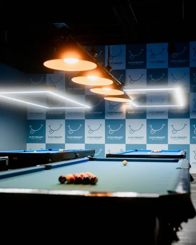 Pool tables under warm pendant lights inside Ponyboat Social Club.
