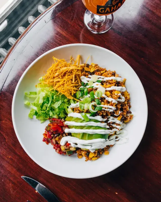 Bowl of a fresh, colourful meal served on a wooden table with a glass of beer.