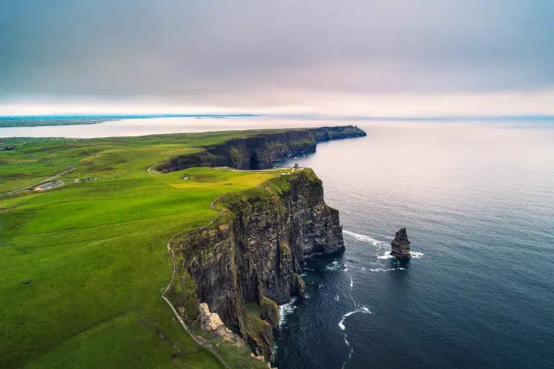 Aerial view of the Cliffs of Moher, where dramatic green cliffs rise above the Atlantic Ocean, with rugged coastal scenery stretching into the distance.